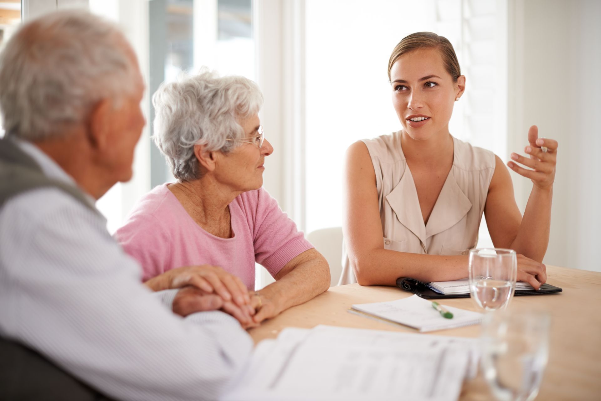 A young professional woman talking to an elderly couple, sitting at a table with documents.
