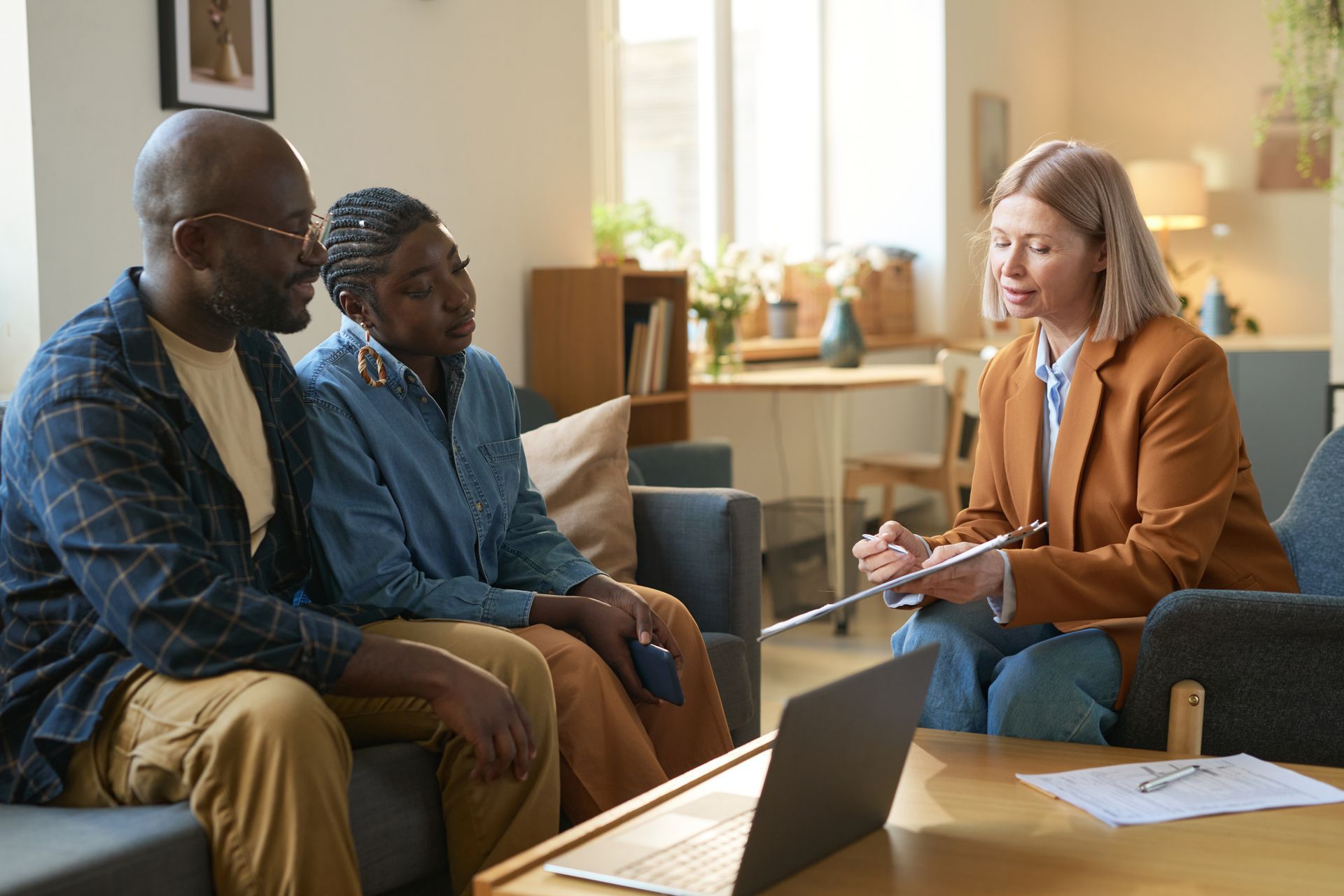 Couple consulting with a professional in a living room, looking at a laptop and documents.
