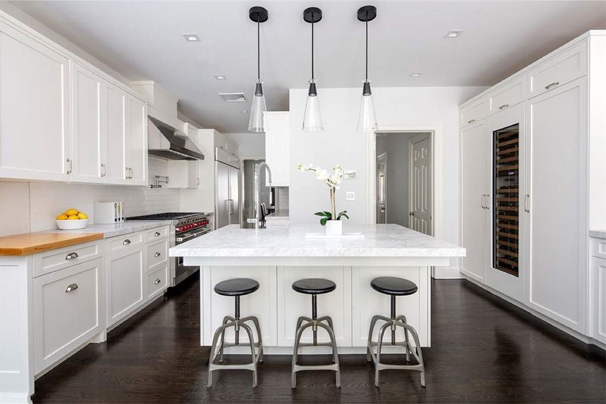 Une cuisine avec des armoires et des tabourets blancs et un grand îlot.