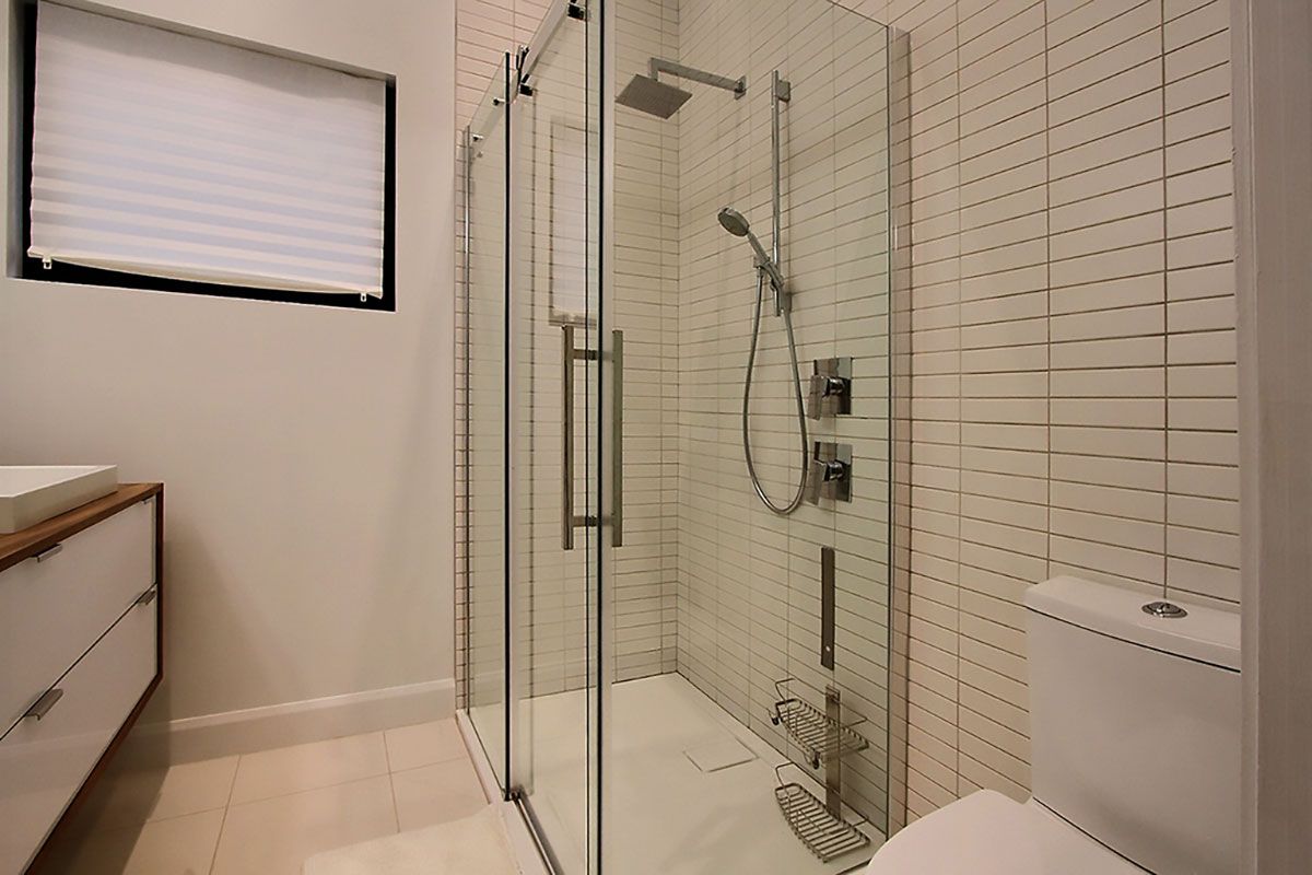 Salle de bains moderne avec douche en verre, murs blancs et toilettes.