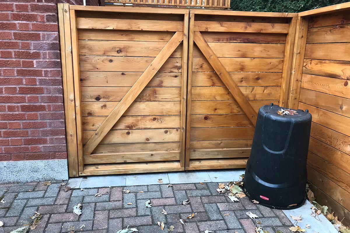 Une clôture en bois avec une poubelle noire devant.