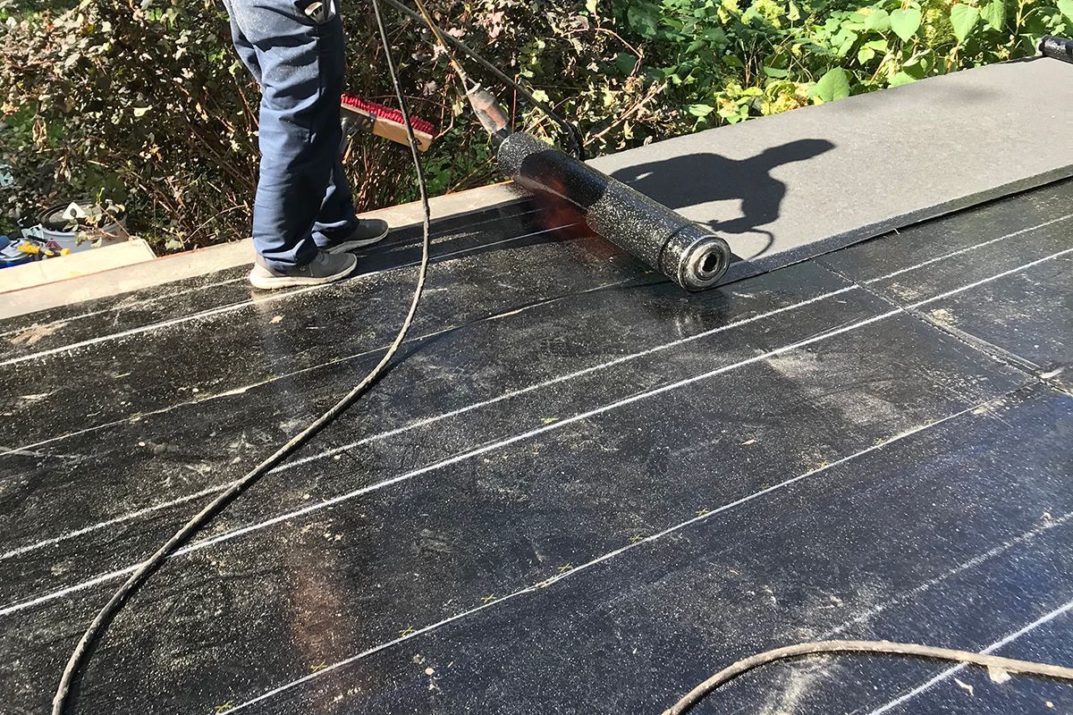 Un homme enroule un rouleau de matériau de toiture sur un toit.