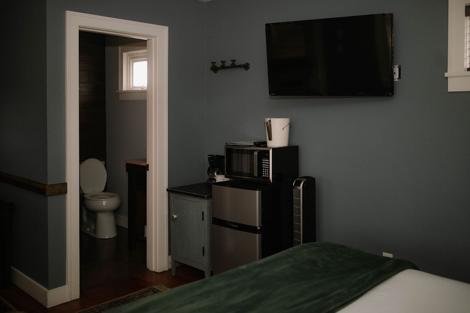 A bedroom with a bed , television , refrigerator , microwave and toilet.