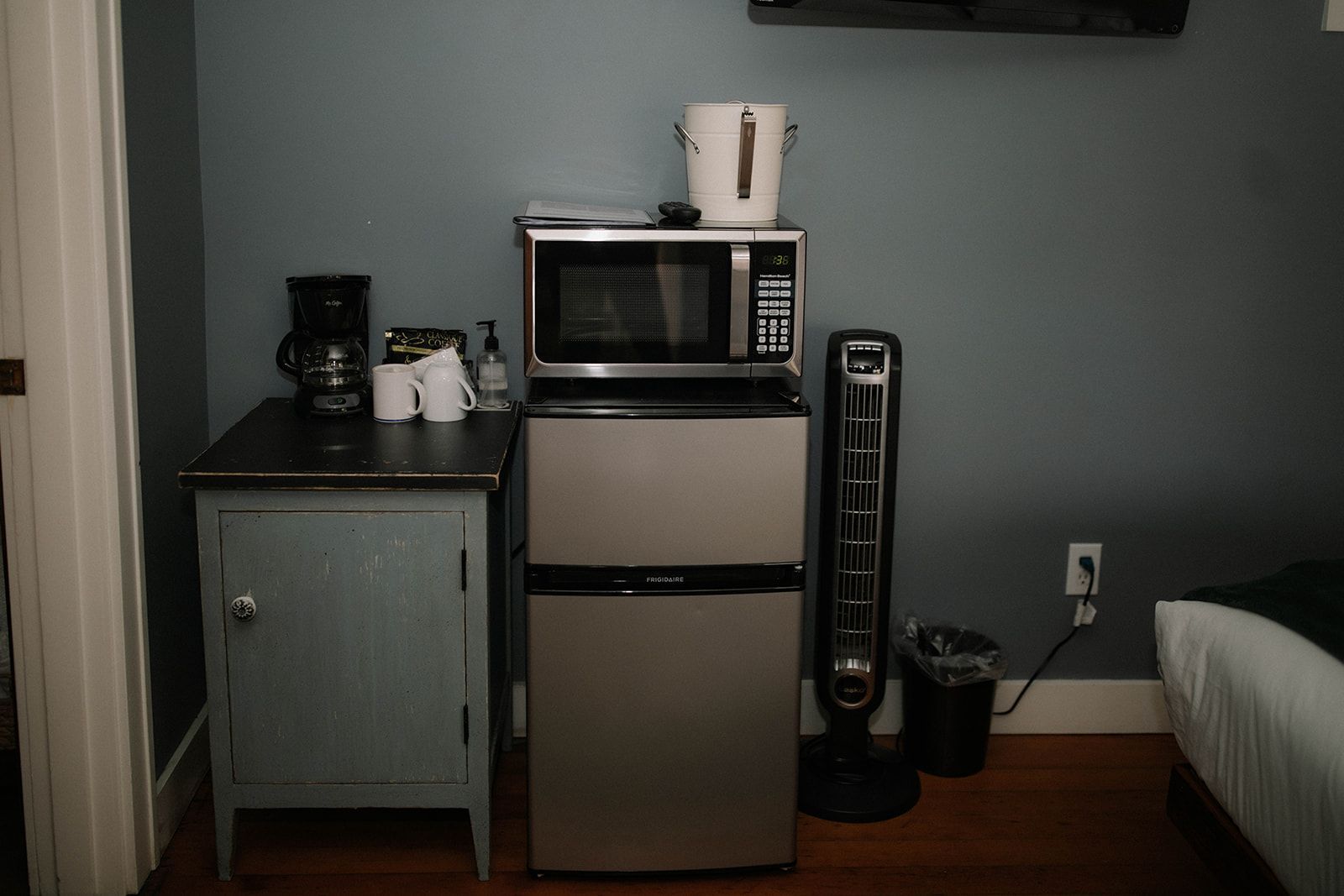 A room with a refrigerator , microwave , coffee maker and fan.