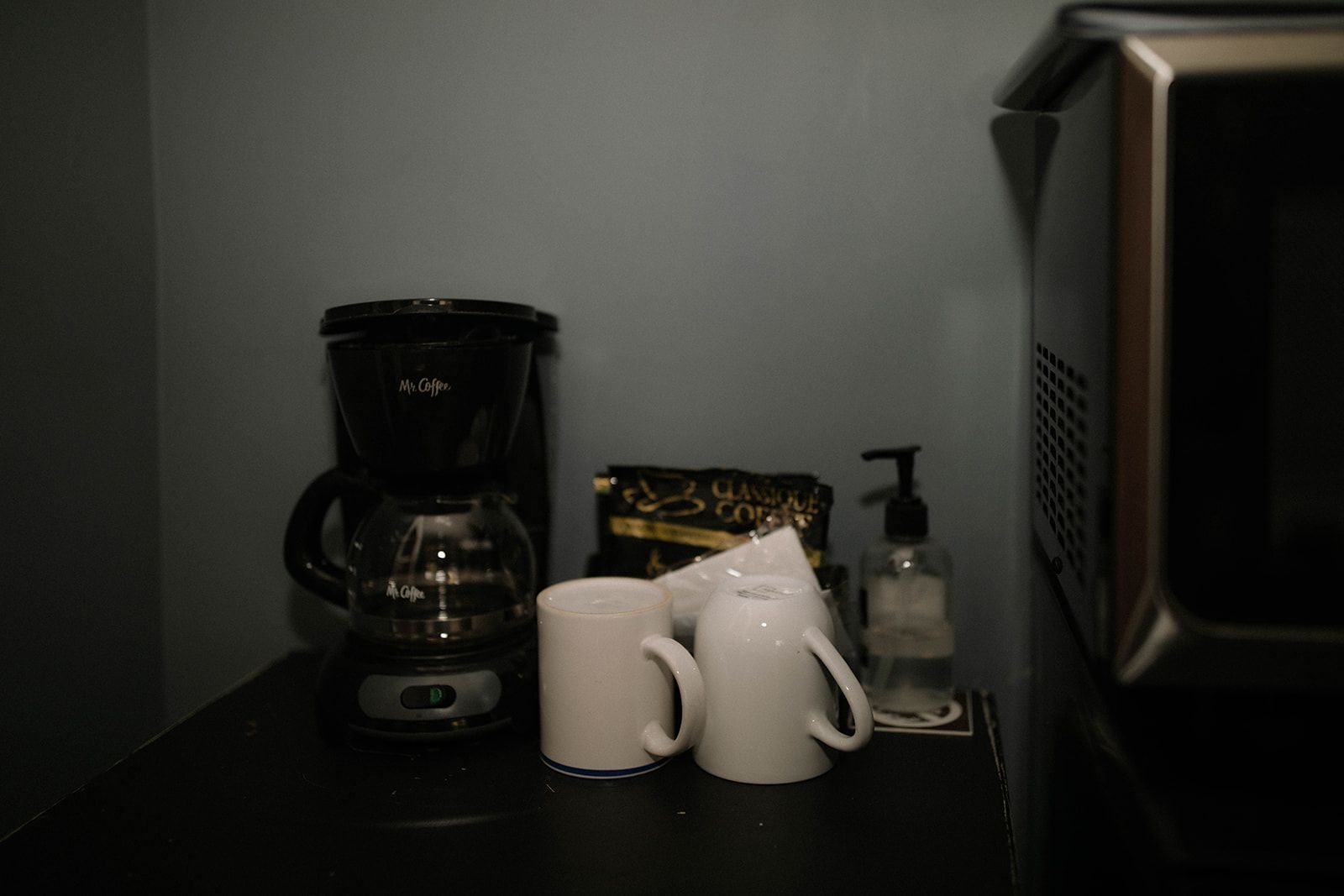 A coffee maker and two mugs are on a counter next to a microwave.