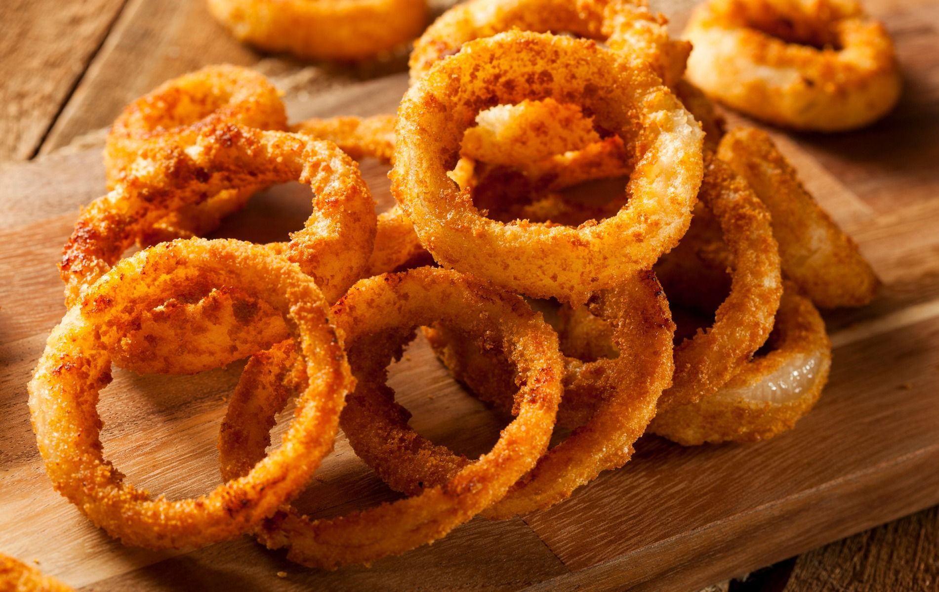 A pile of onion rings on a wooden cutting board.