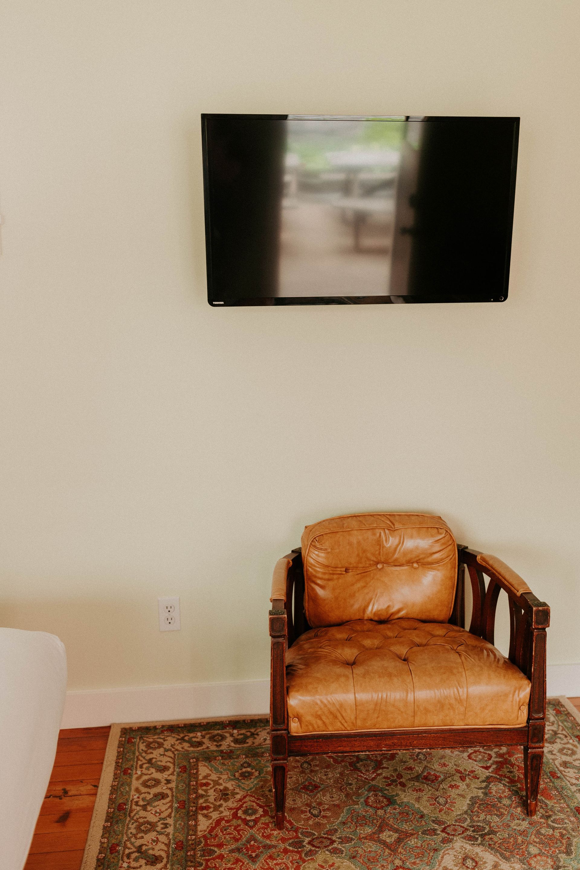 A brown leather chair is sitting next to a flat screen tv on a wall.