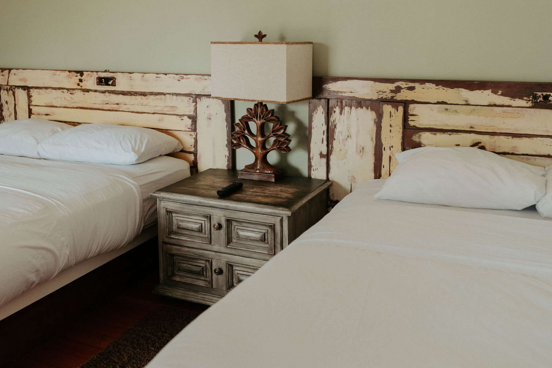 A bedroom with two beds , a nightstand and a lamp.