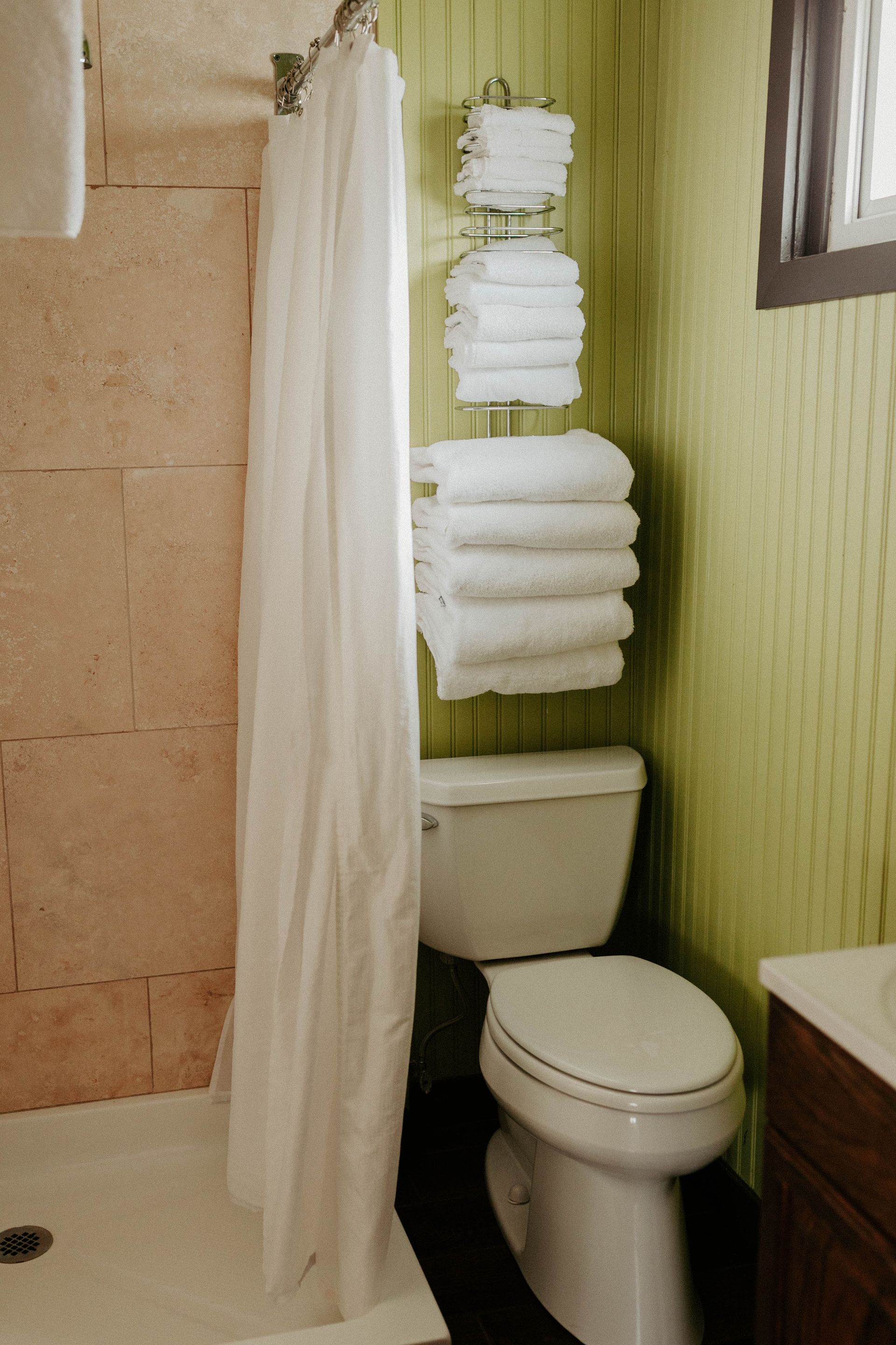 A bathroom with a toilet , shower and stacks of towels on the wall.