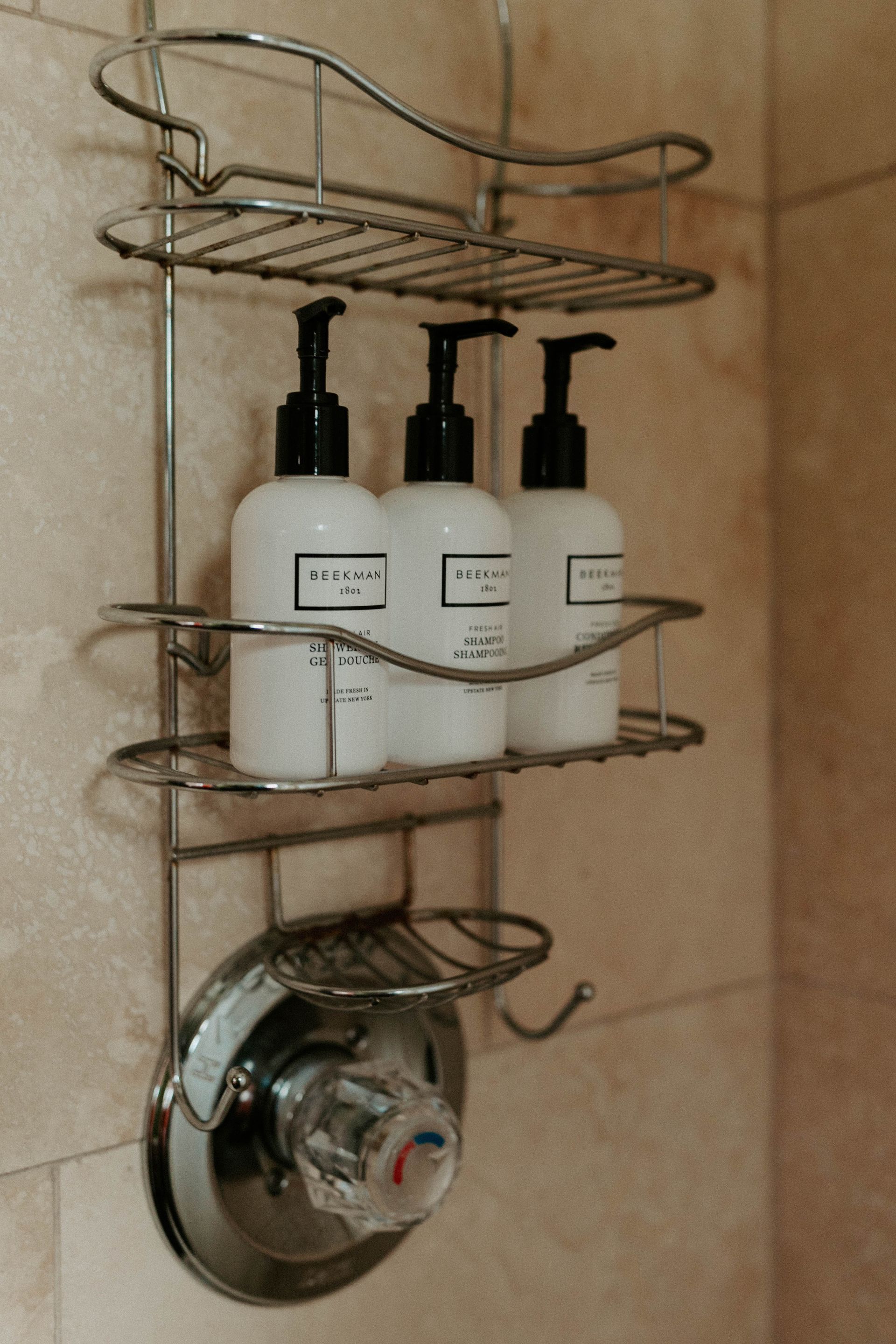 Three bottles of lotion are sitting on a shelf in a shower.
