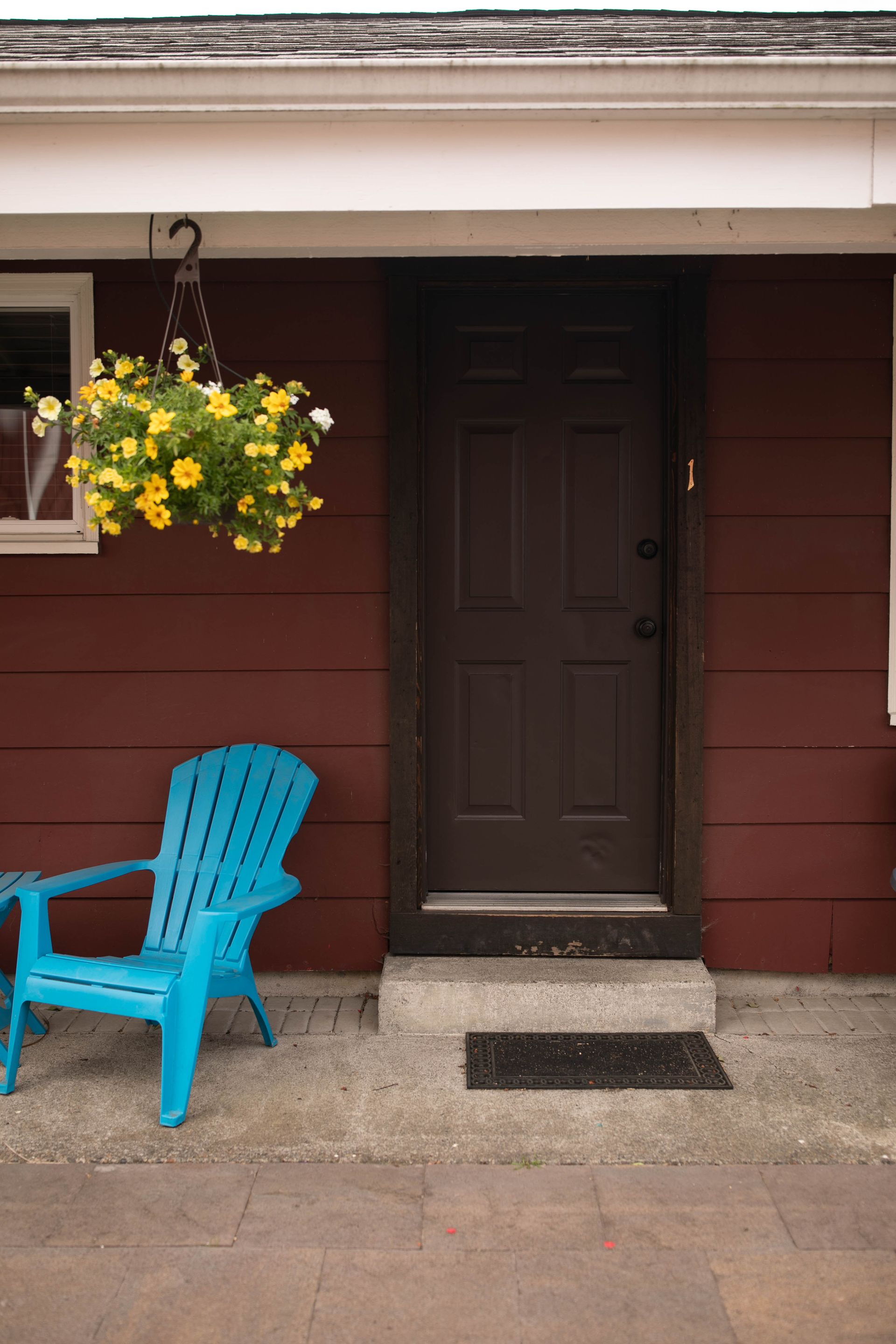 A blue chair and a basket of yellow flowers are on the porch of a house.