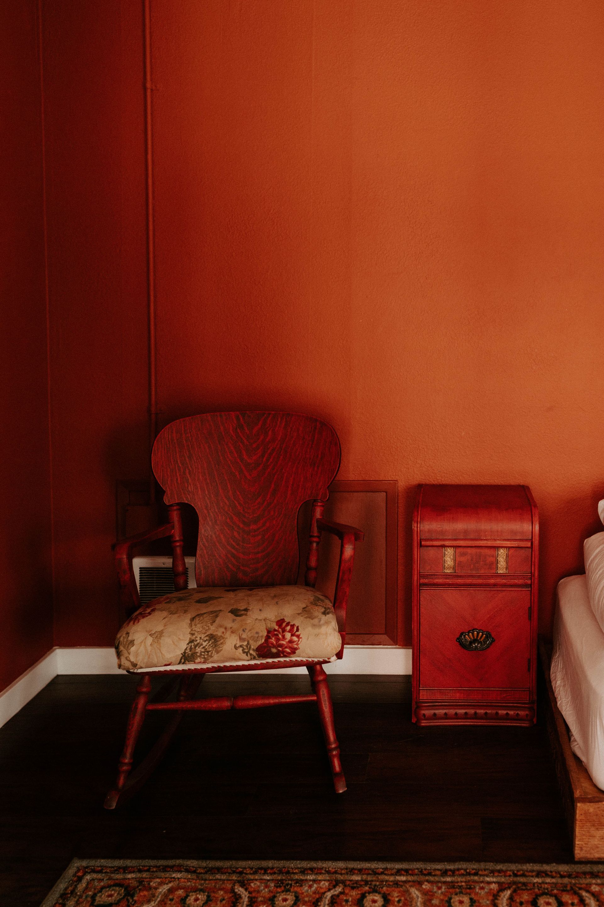 A red chair is sitting in a corner of a room next to a red nightstand.
