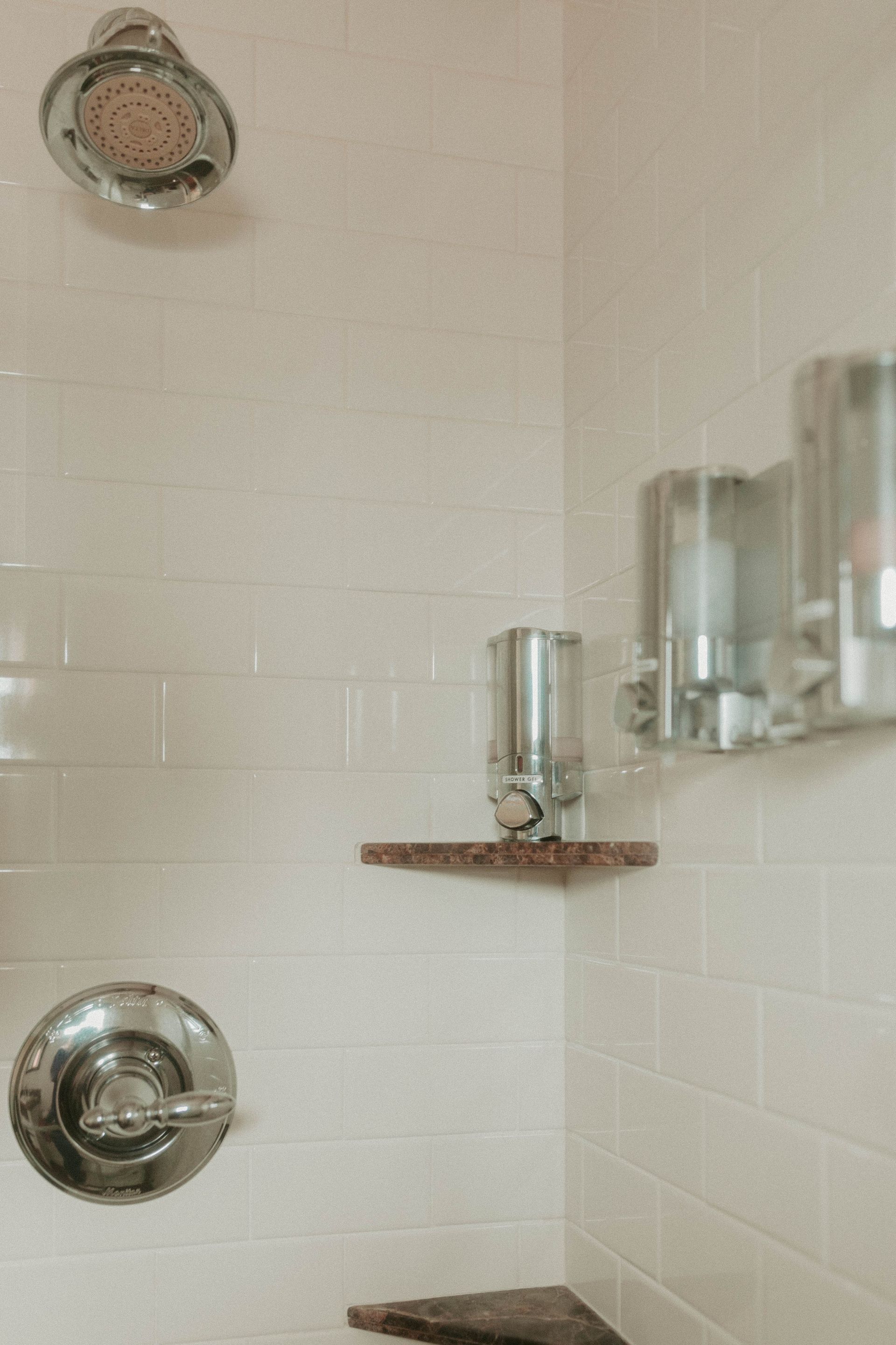 A bathroom with a shower head , soap dispensers , and a mirror.