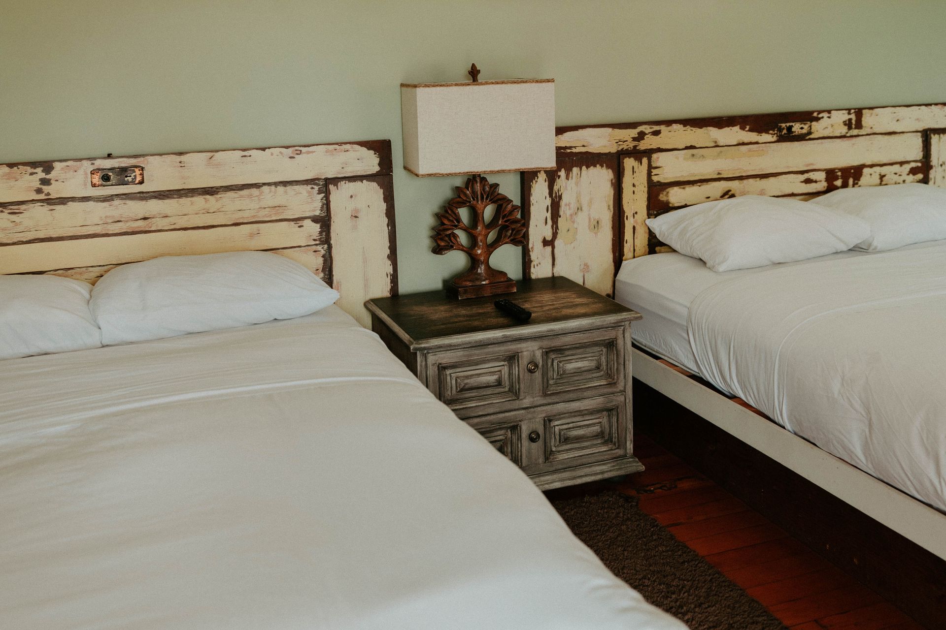 A hotel room with two beds , a nightstand and a lamp.