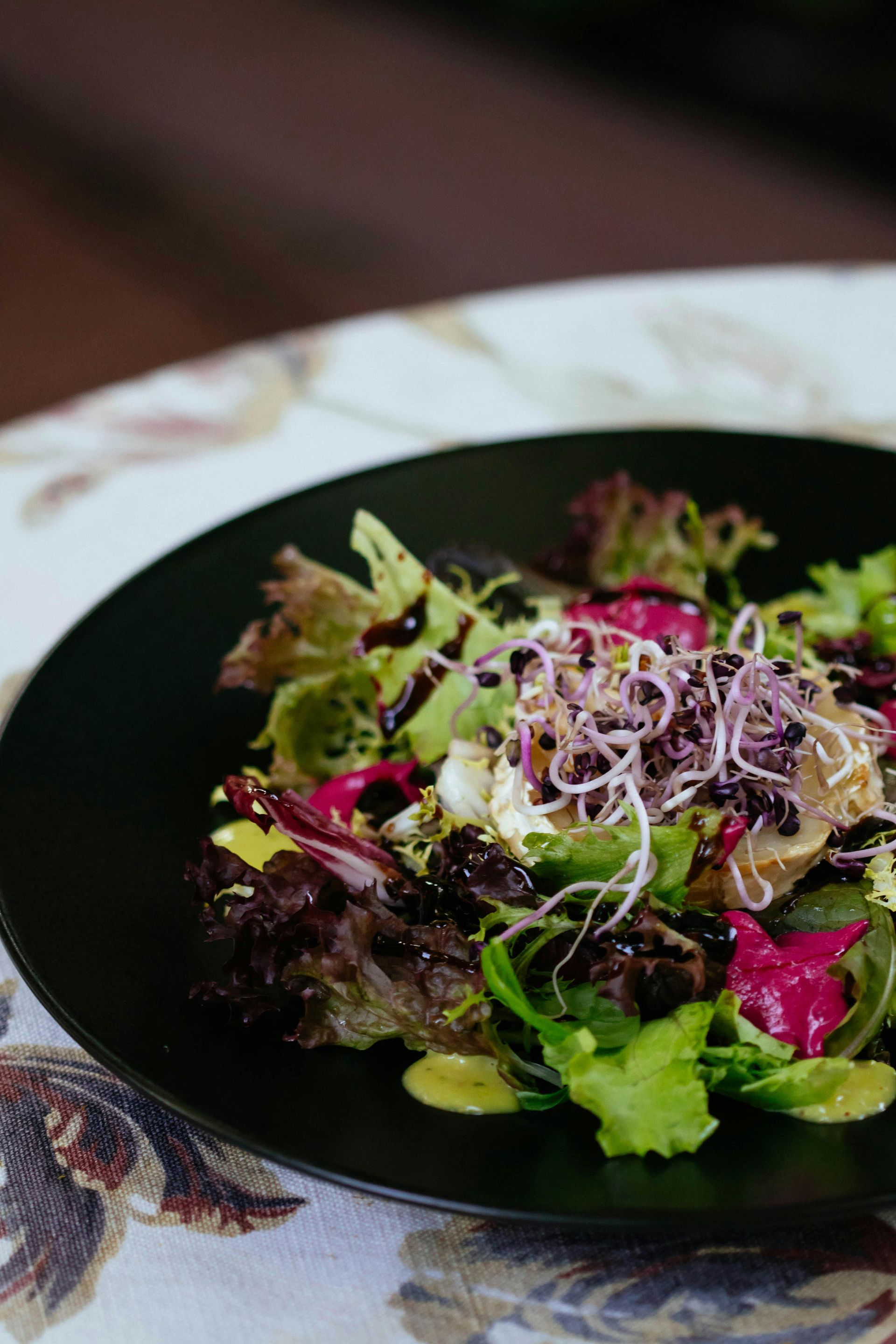 A close up of a salad on a black plate on a table.