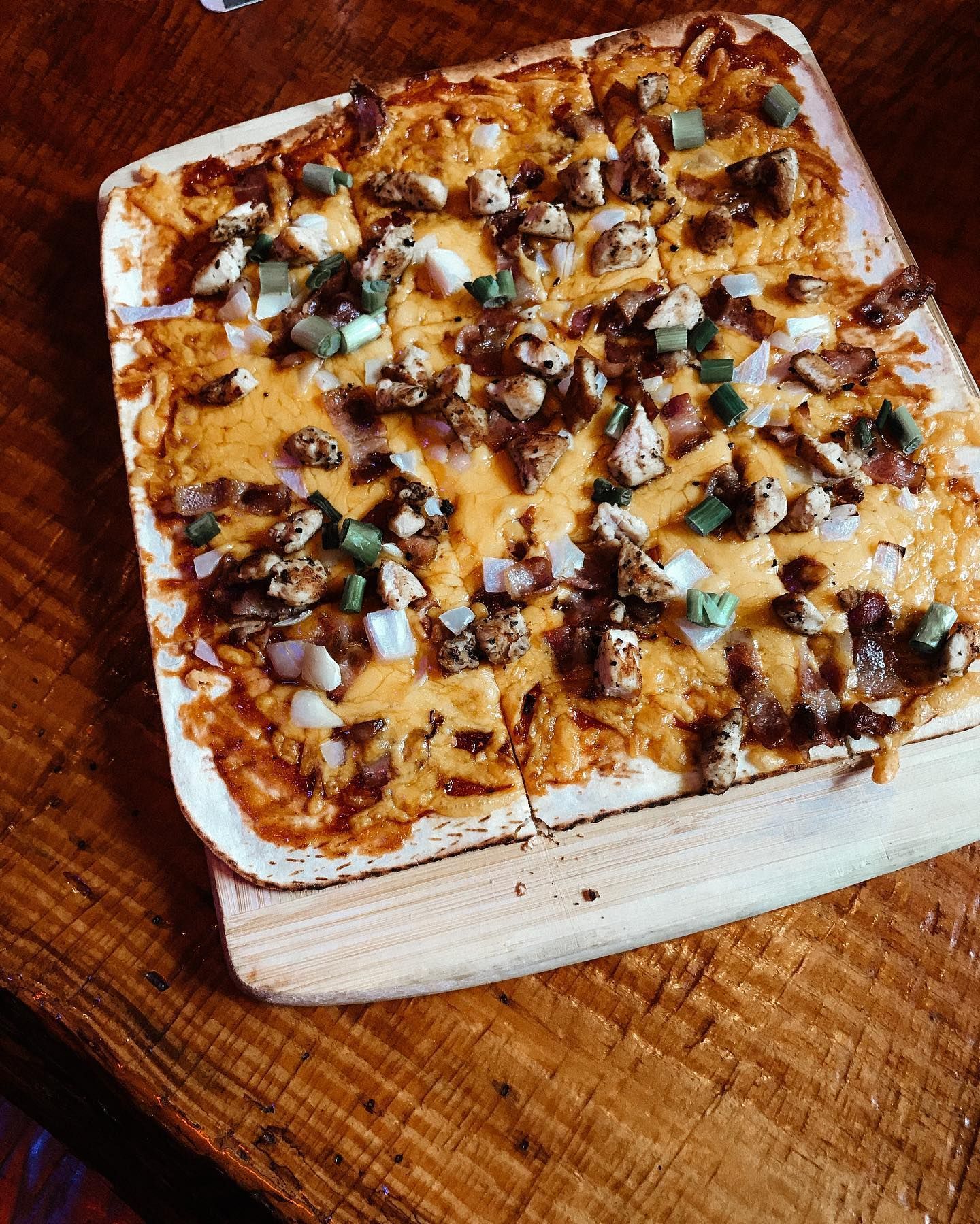 A pizza is sitting on a wooden cutting board on a wooden table.