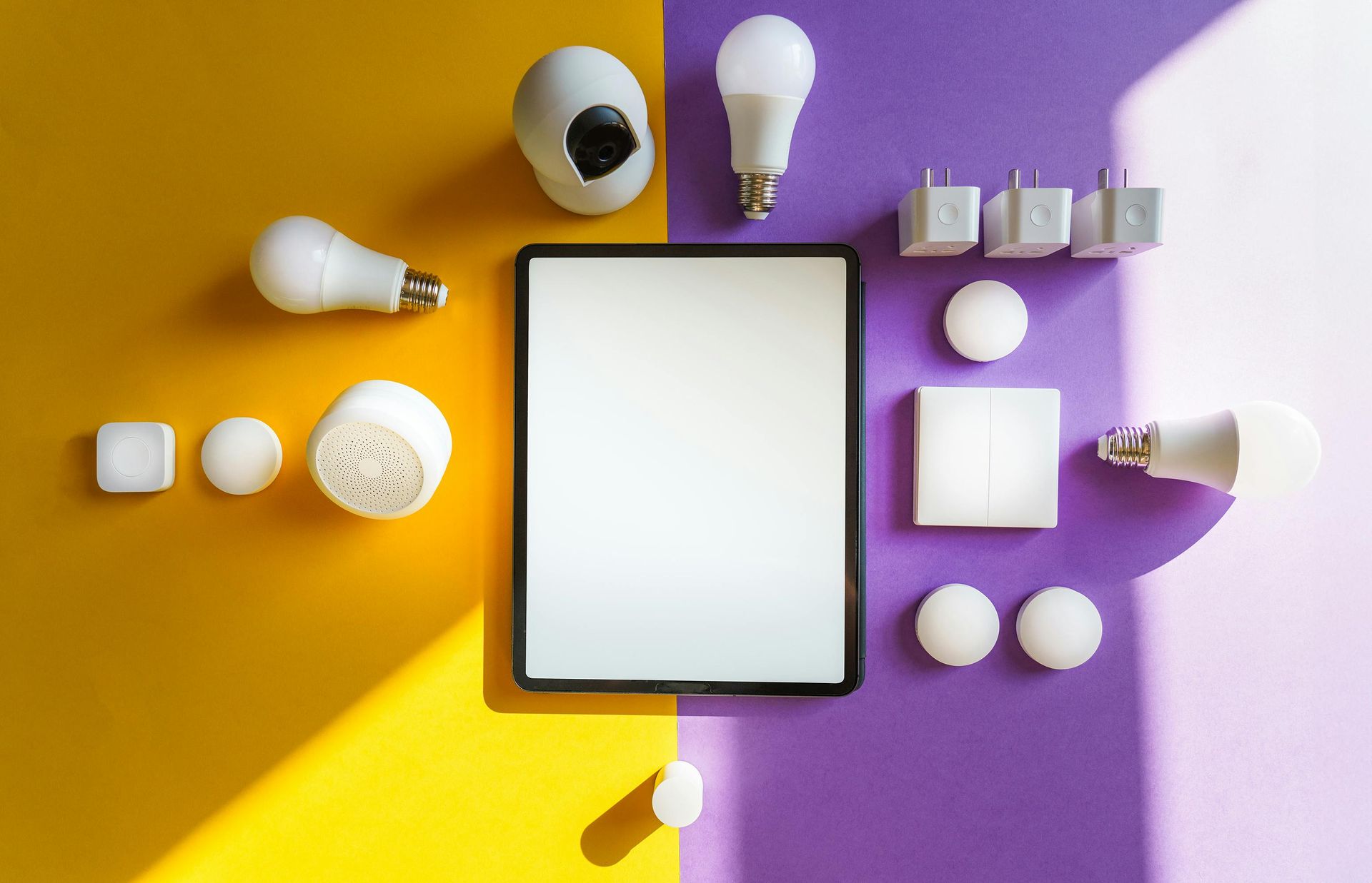 Smart home devices, including lights, plugs, and a tablet, arranged on yellow and purple surfaces.