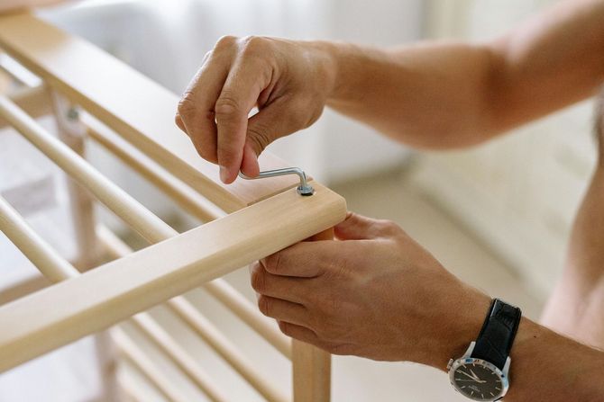 Person assembling a light wooden crib, attaching metal hardware.