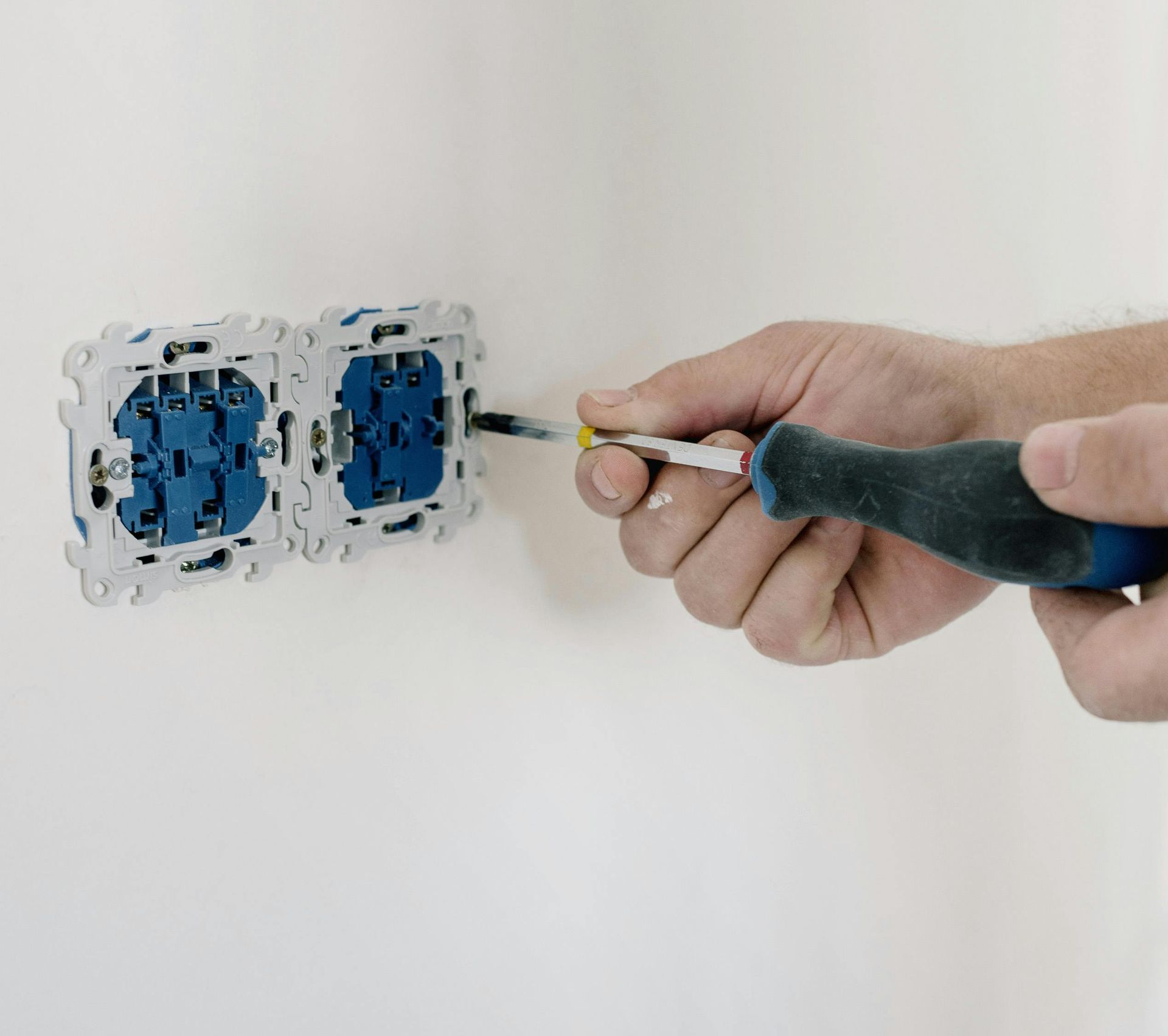 Person using a screwdriver to install a blue electrical outlet on a white wall.