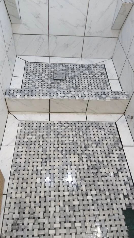 Mosaic-tiled shower with two low steps and a small square drain cover on the back wall.