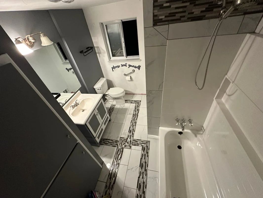 Small white bathroom with tub, vanity, mirror, and tiled floor in grayscale lighting