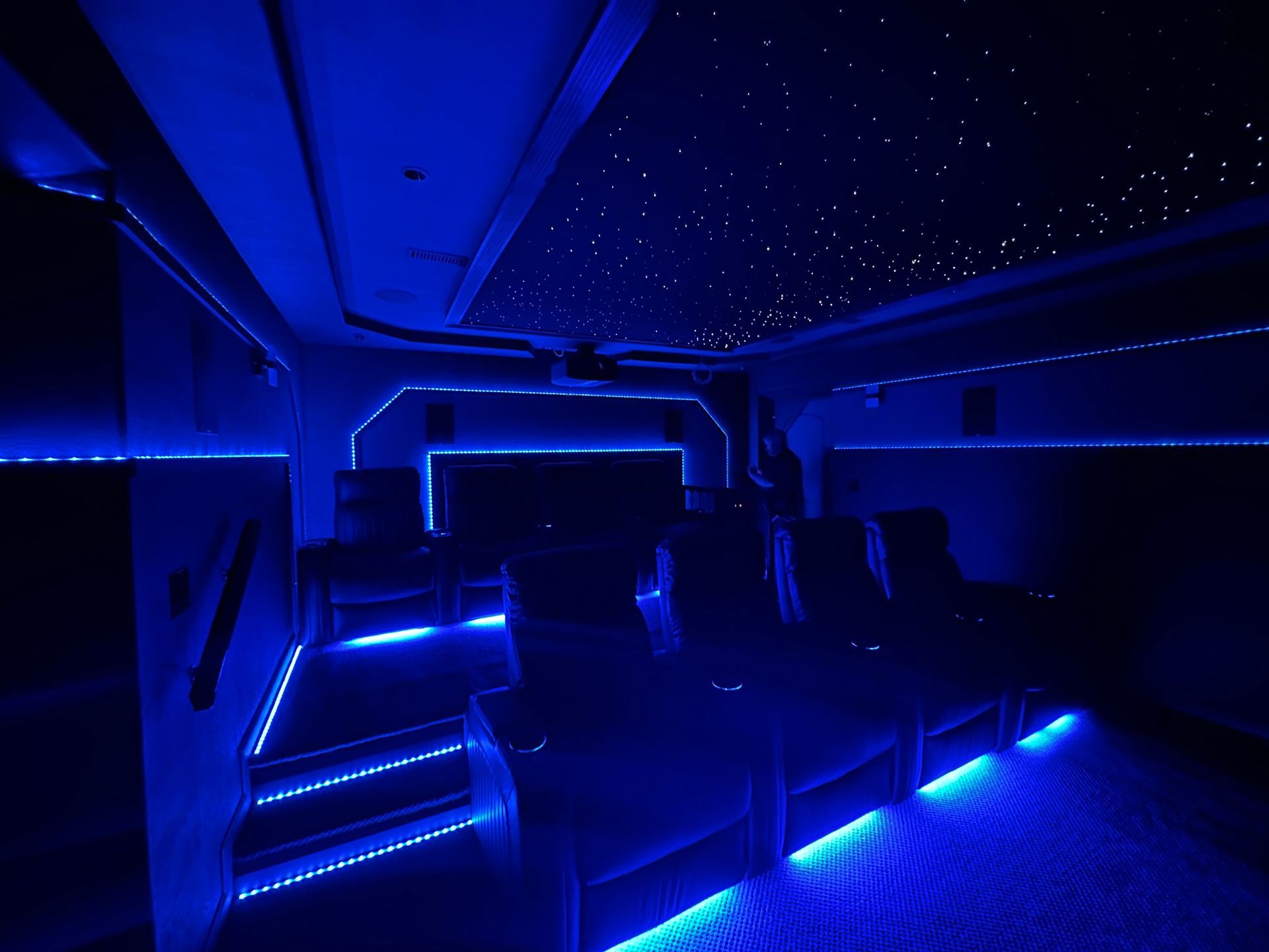 Blue-lit modern lounge with starry ceiling lights and stairs glowing along the aisle