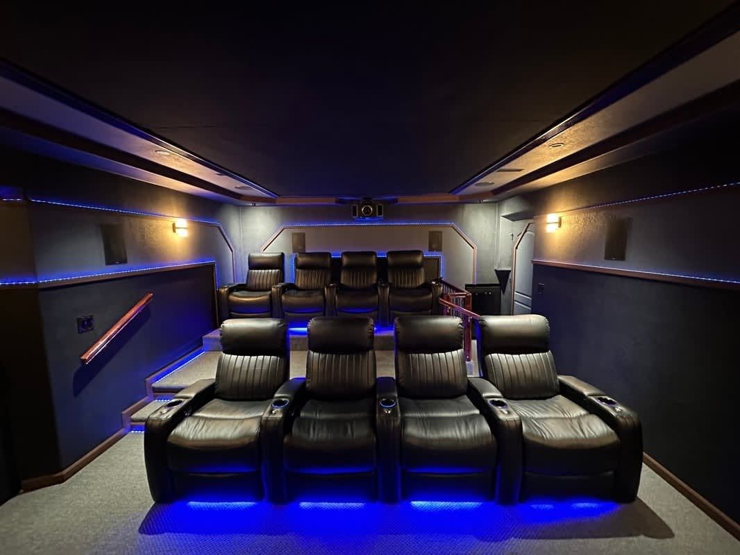 Luxury home theater with black leather recliners, blue accent lighting, and a large screen at the front