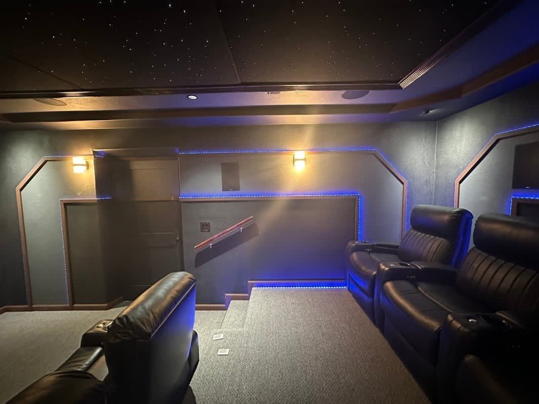 Modern lounge with black leather seating, blue accent lighting, and a stairway in a dim interior.