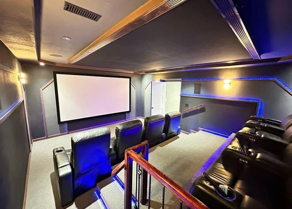 Small home theater with rows of black recliners, a large projection screen, and blue accent lighting.