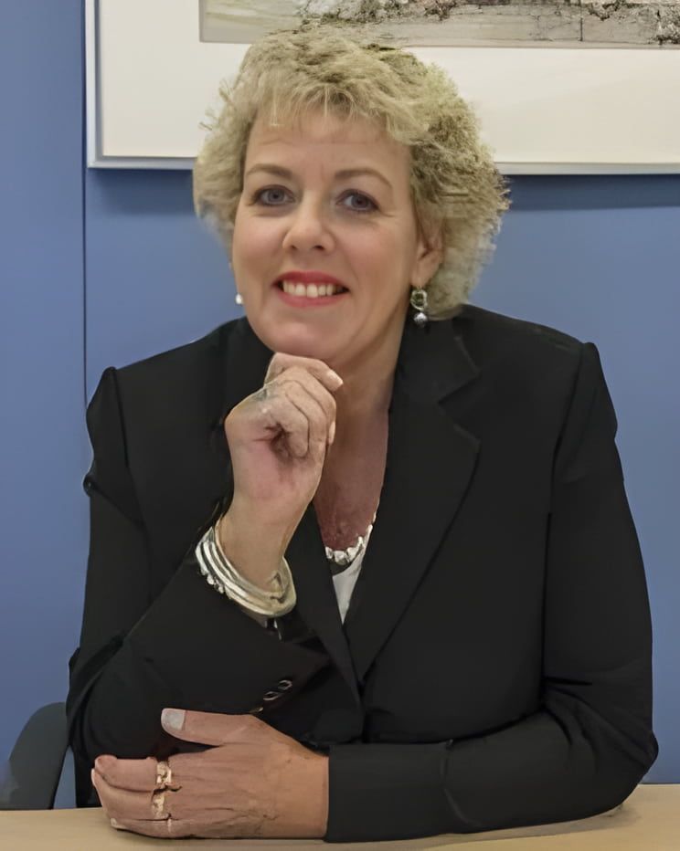 A woman in a black suit is sitting at a table with her hand on her chin — Linda Emery & Associates In Gosford, NSW