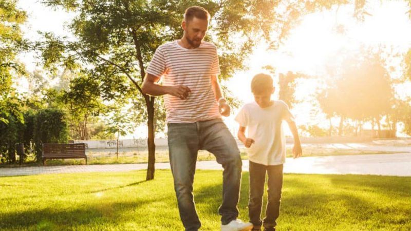 A Man and A Boy Are Playing with A Soccer Ball in A Park — Linda Emery & Associates In Gosford, NSW