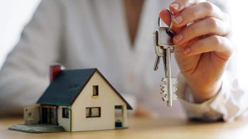 A Woman Is Holding a Pair of Keys in Front of A Model House — Linda Emery & Associates In Gosford, NSW