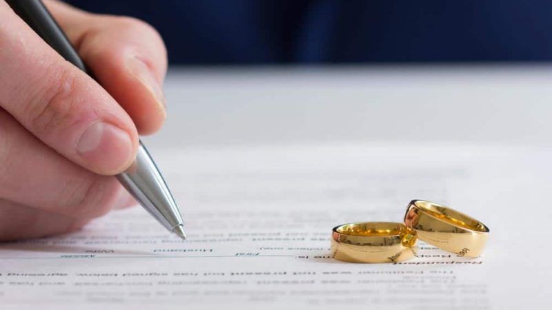 A Person Is Writing on A Piece of Paper Next to A Pair of Wedding Rings — Linda Emery & Associates In Gosford, NSW