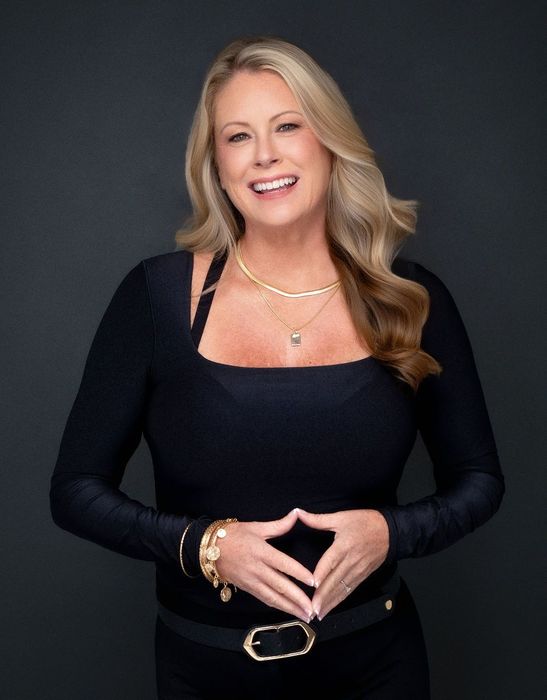 Person working at a light wood desk with plants, books, and a white vase on a stool.