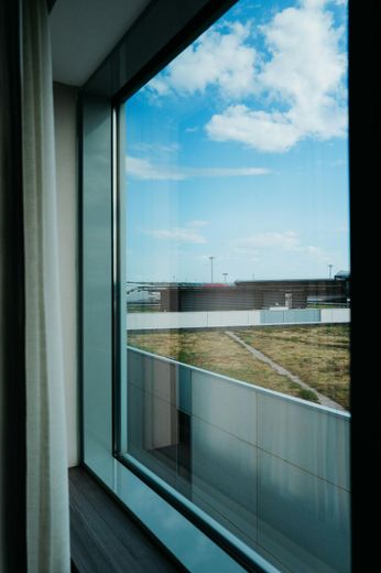 View from a window, blue sky with clouds. Outside, a modern building and grassy area.