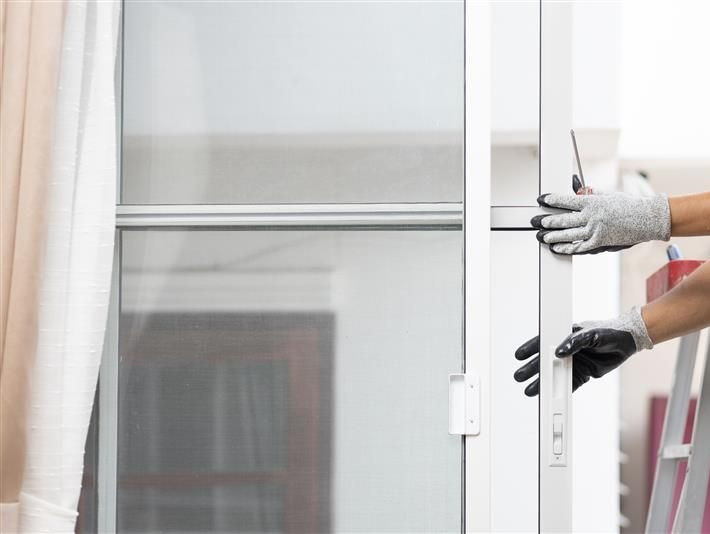 Person in gloves installing a white screen door, outdoors, with ladder.
