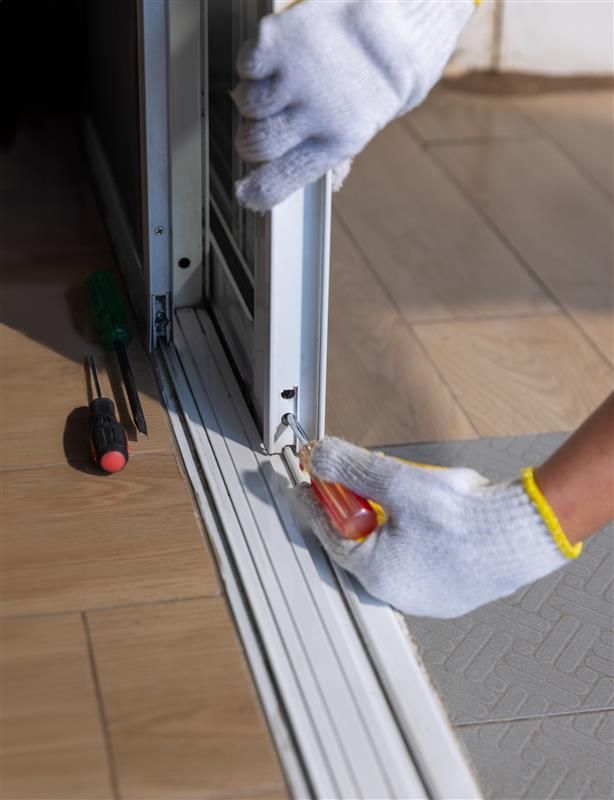 Person in gloves using a screwdriver to adjust a sliding door mechanism.