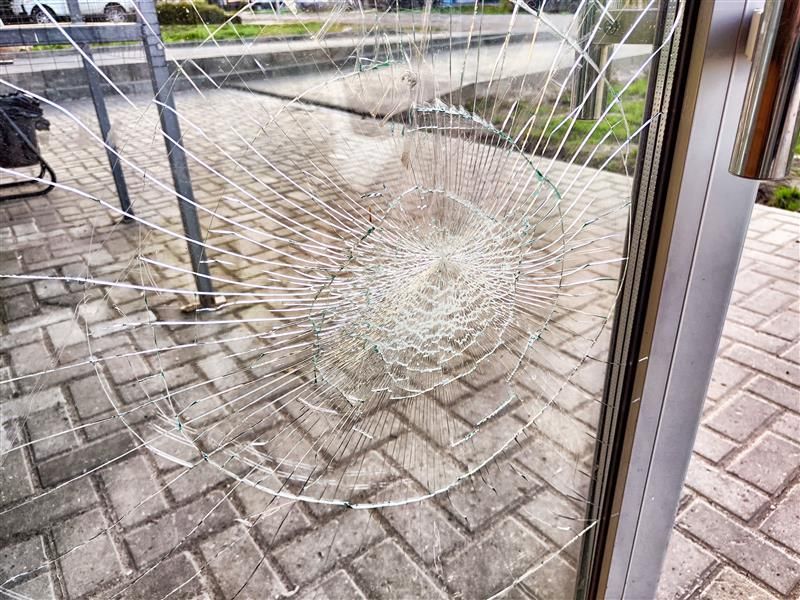 Broken glass window in a building entrance. The glass has a spiderweb-like crack pattern.