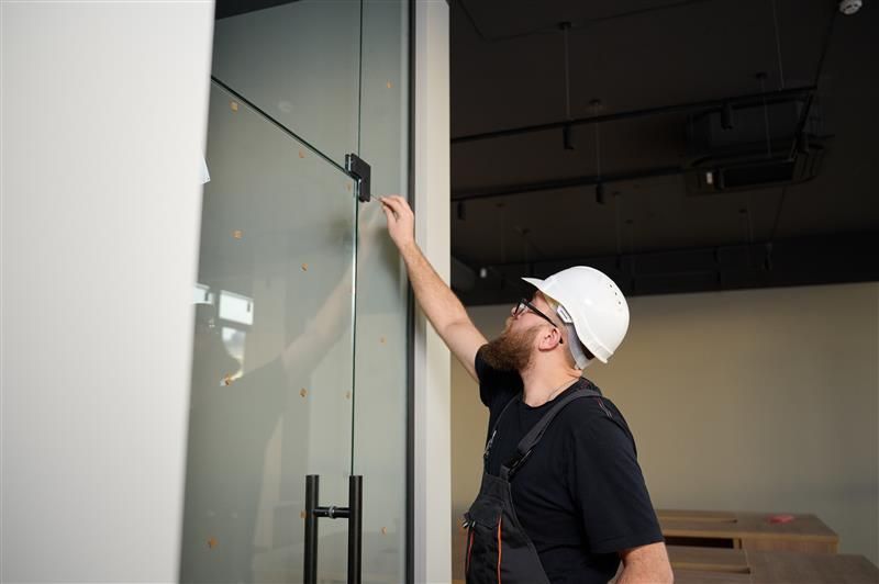 Construction worker with white hard hat inspecting a glass door in a building.