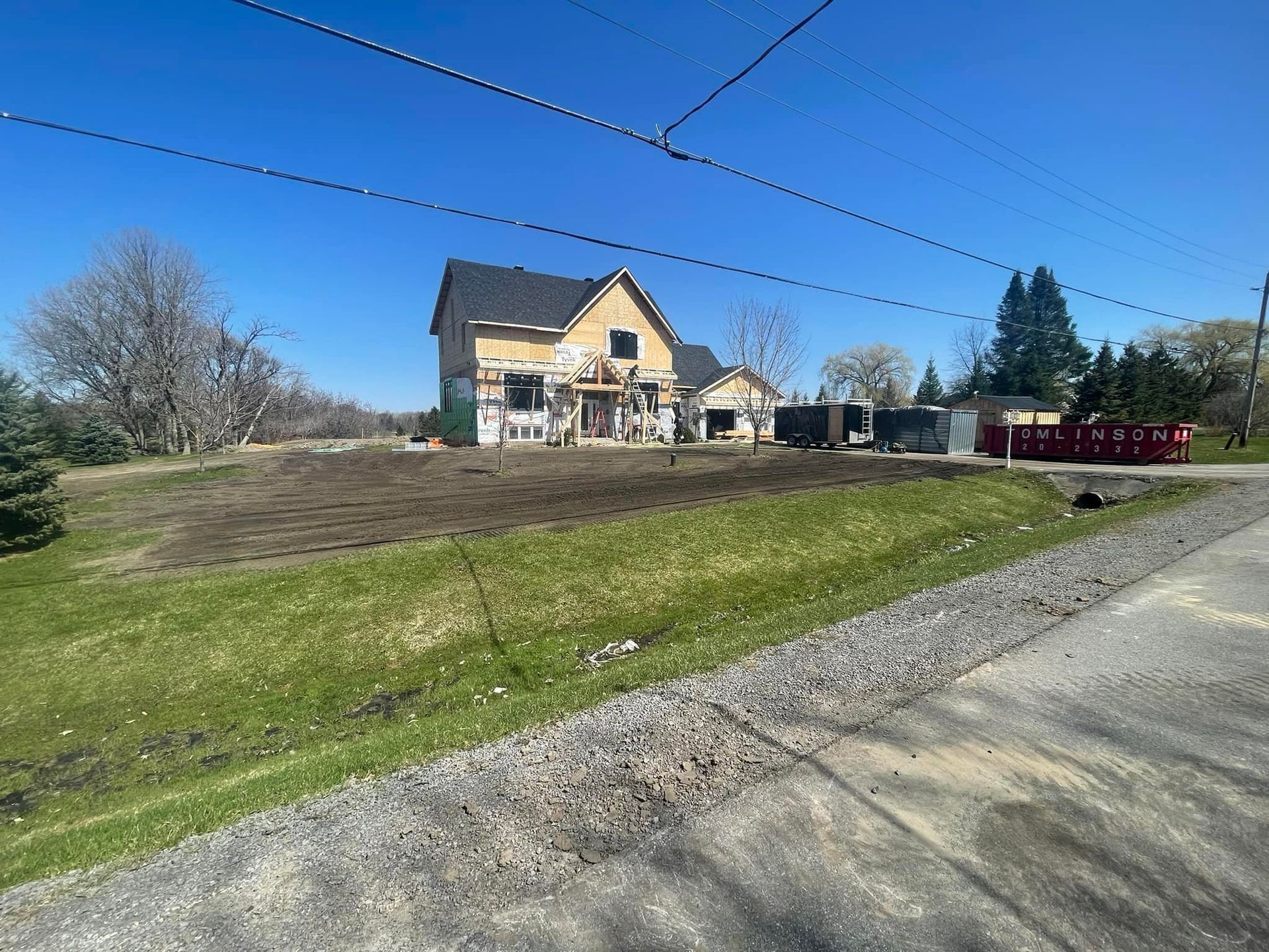 House under construction; tan siding, black roof, with brown dirt lawn in front, blue sky.