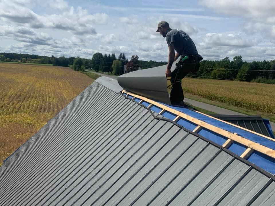 Roofer on a metal roof placing insulation. Cloudy sky, field in background.