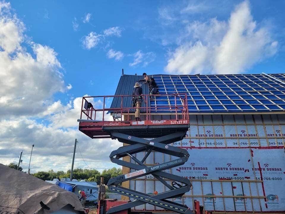 Two workers on scissor lift installing solar panels on a building's roof, under blue sky.