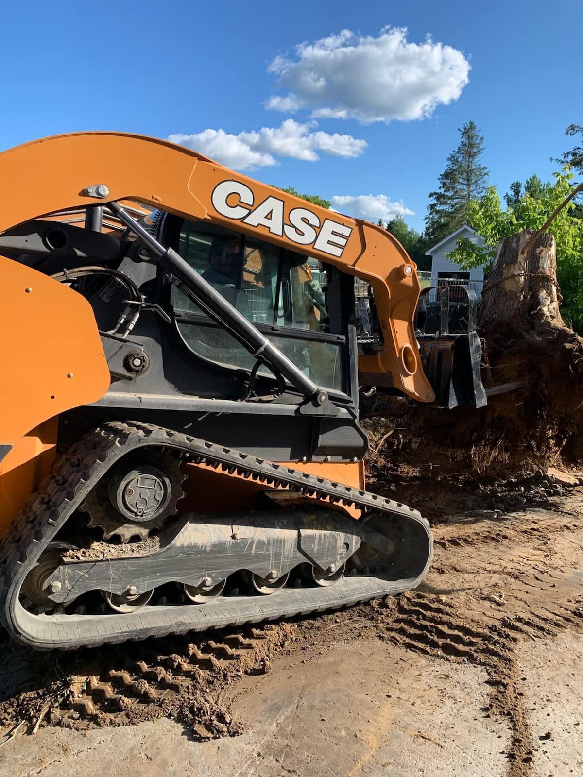 Orange CASE track loader removing a tree stump in a sunny outdoor setting.