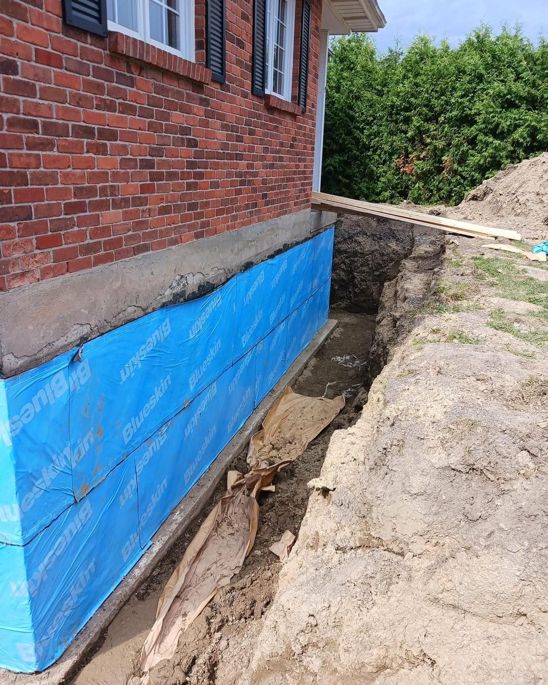 Foundation of a brick house with blue waterproofing membrane; excavated trench.