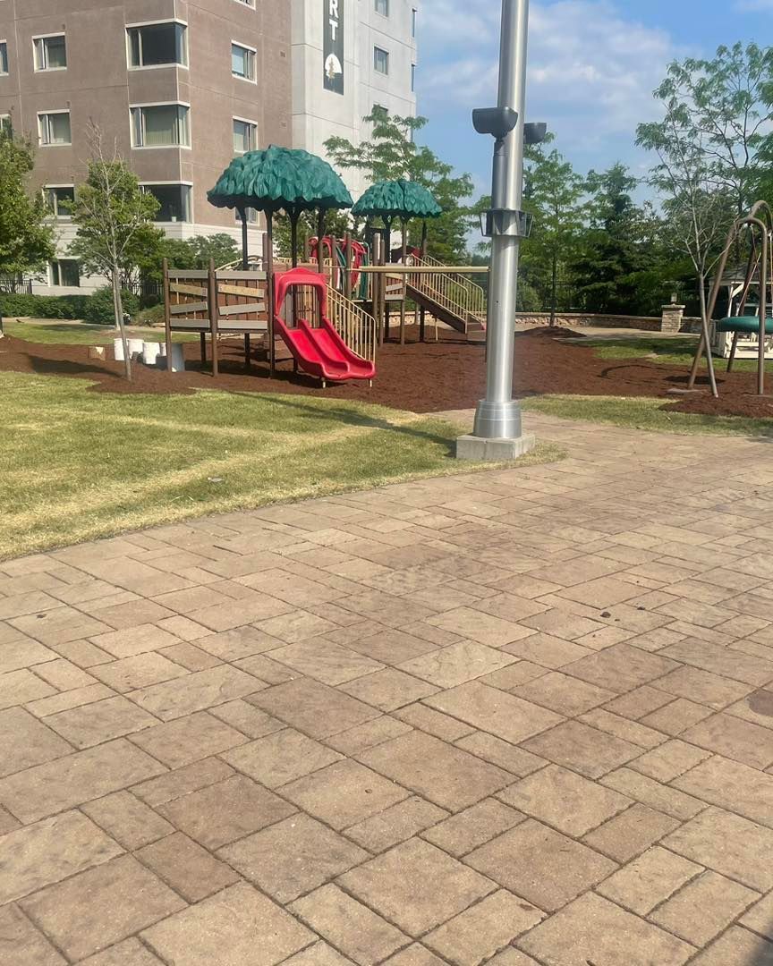A playground with a red slide and brown mulch, in front of a light-colored building.