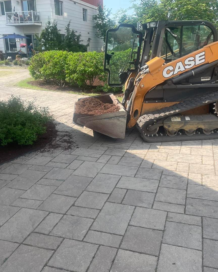 An orange Case skid steer with bucket on a brick driveway removing mulch.