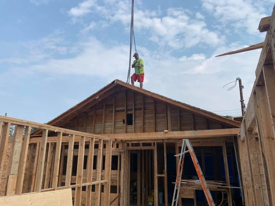 Construction worker on roof framing a house under a partly cloudy sky.