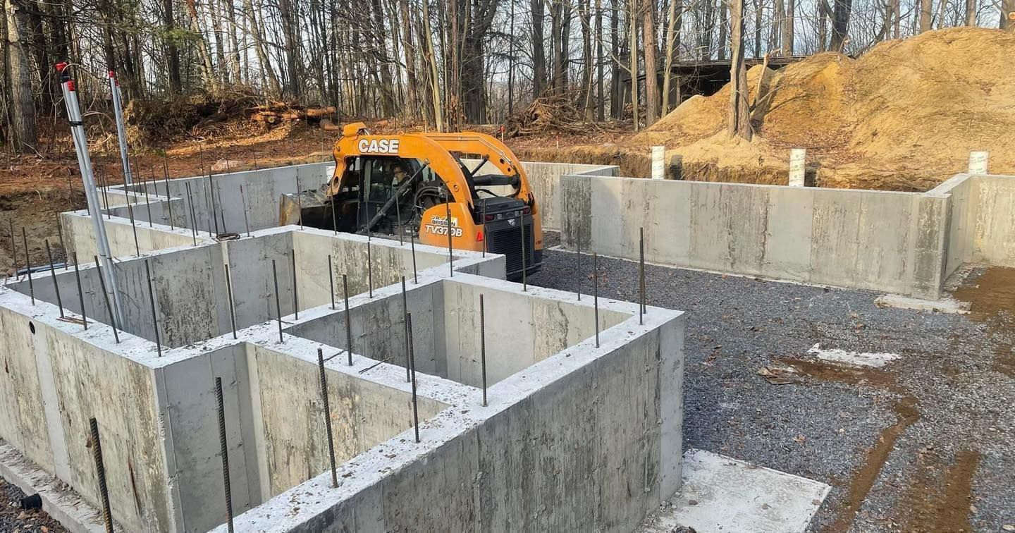 Foundation of a house under construction with an orange skid steer in the middle.