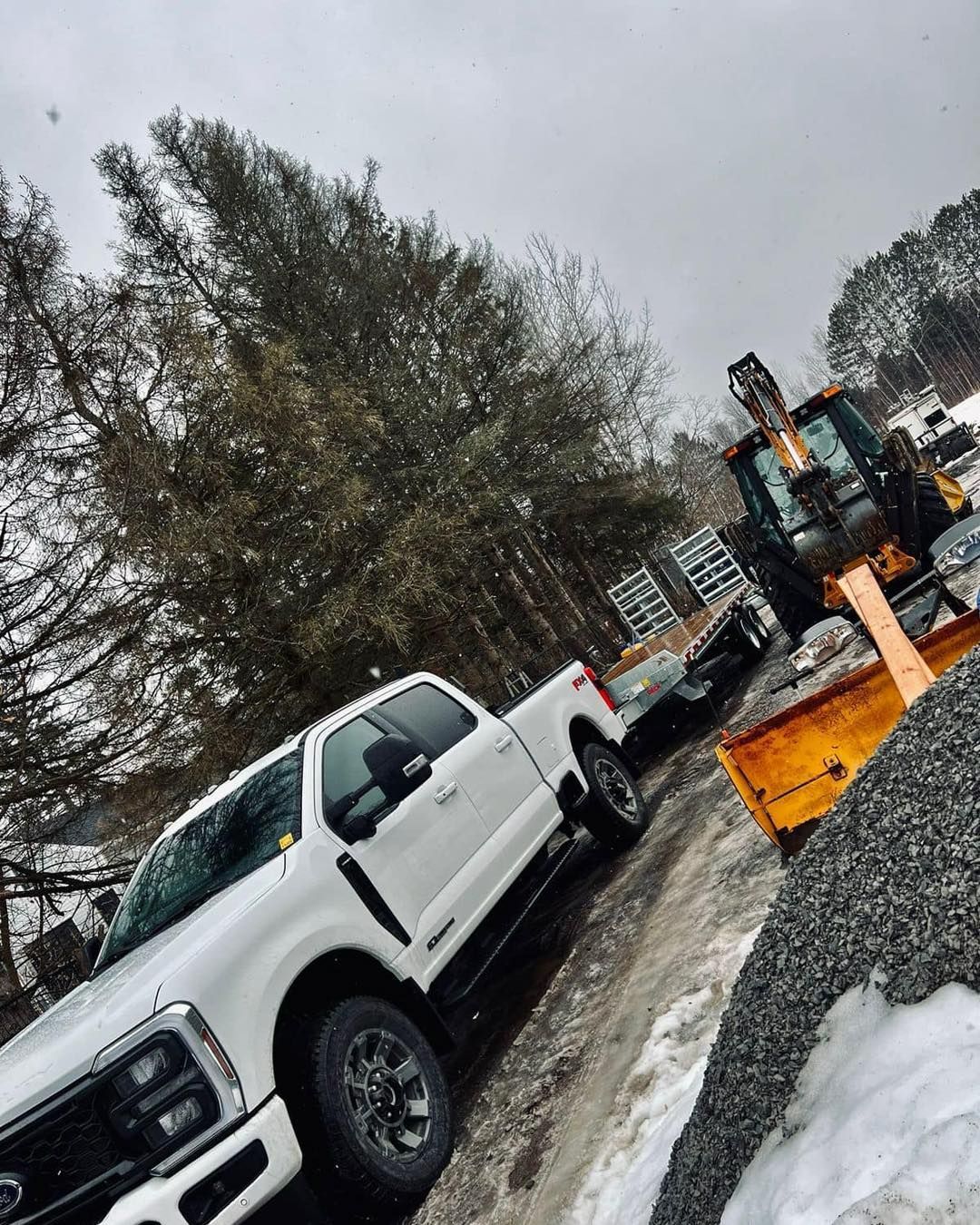 White truck towing a trailer with construction equipment in a snowy, outdoor setting.