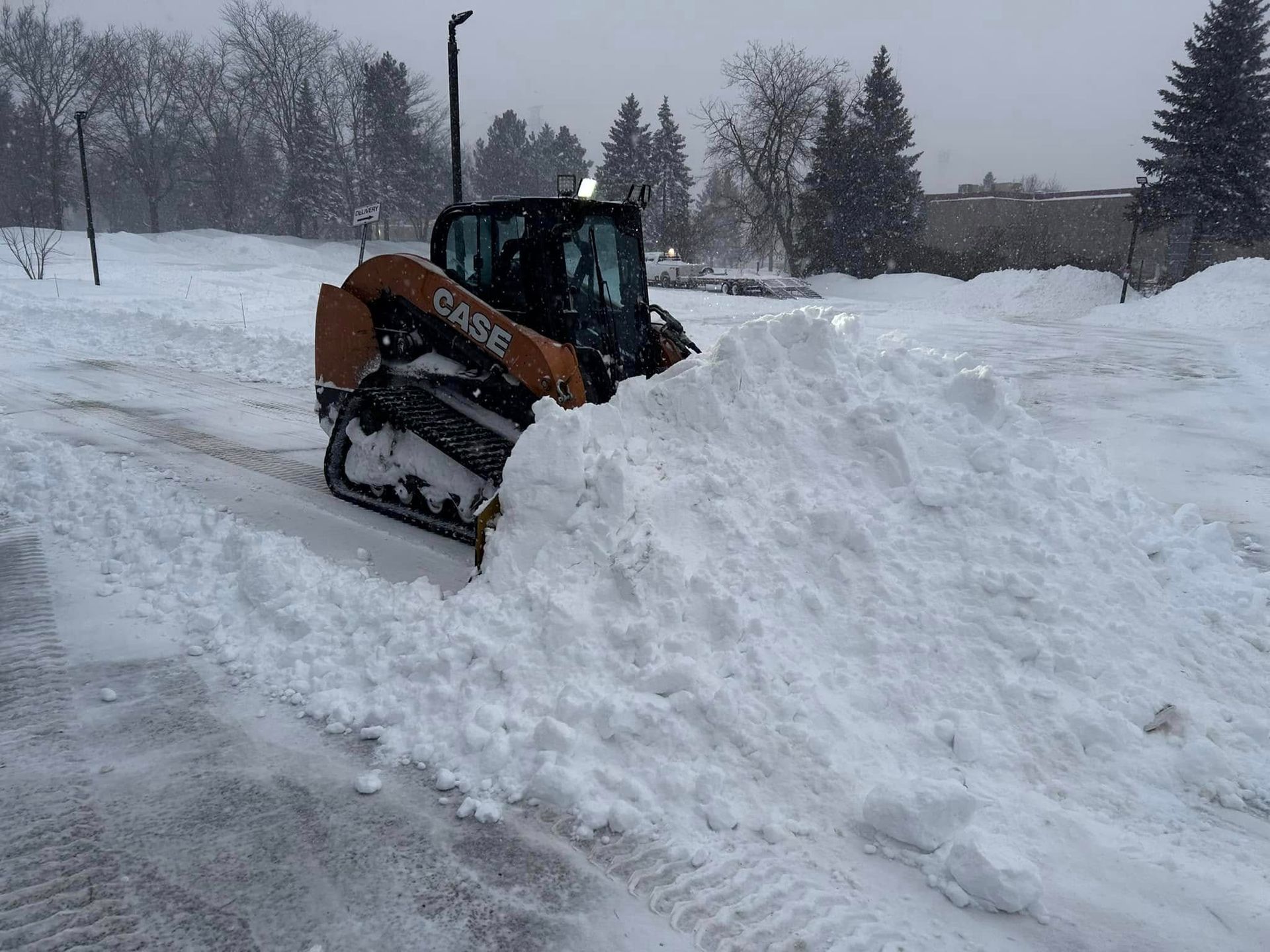 Snowplow clearing snow from a parking lot during a winter storm.